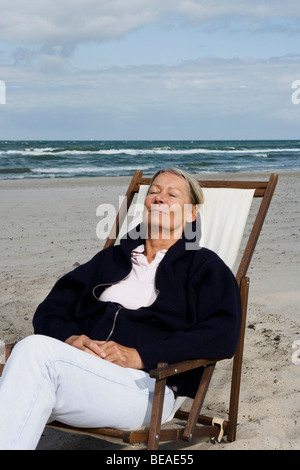 A senior woman reclining dans une chaise longue sur la plage Banque D'Images