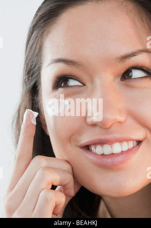 Mixed Race woman applying cream sous les yeux Banque D'Images