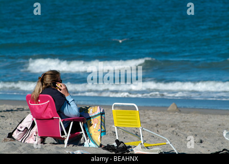 Femme assise sur une plage de sable à l'aide d'un mobile, Jupiter, Floride Banque D'Images