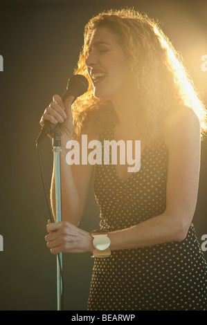 Hispanic woman singing into microphone sur scène Banque D'Images