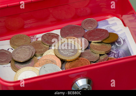 Une petite caisse verrouillable métal rouge boîte contenant de l'argent britannique avec les pièces de monnaie dans l'accent Banque D'Images