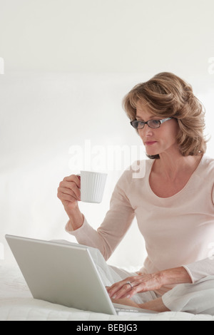 Femme au travail sur un ordinateur portable sur le lit Banque D'Images