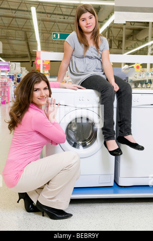 Fille assise sur une machine à laver à côté de sa mère dans un supermarché Banque D'Images