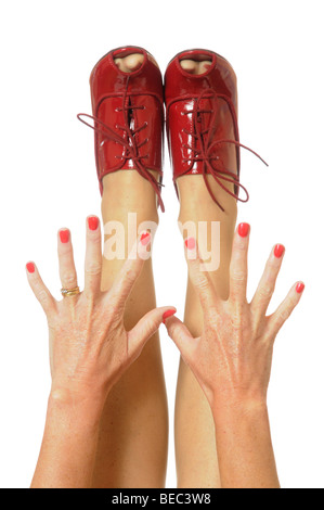 Les ongles peints en rouge avec des mains tendues à red high heeled shoes Banque D'Images