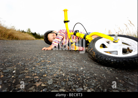 Garçon enfant vélo bicyclette sur la route de campagne avec casque de vélo, d'une chute, accident Banque D'Images