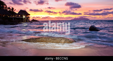 Roche de granit typique des Seychelles sur la plage au crépuscule près de glacis, Sunset Beach Resort à l'arrière, l'île de Mahé, Seychelles Banque D'Images