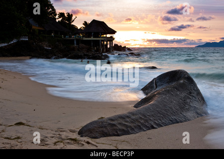 Roche de granit typique des Seychelles sur la plage au crépuscule près de glacis, Sunset Beach Resort à l'arrière, l'île de Mahé, Seychelles Banque D'Images