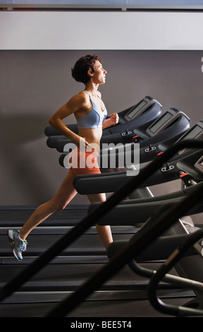 Fin des années 20 femme s'exécutant dans un healthclub sur un tapis roulant. Banque D'Images