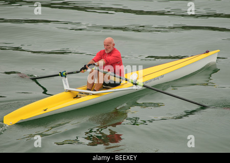 Un homme d'âge moyen en bonne santé mettre en place seul dans une rame solo monoplace scull aviron canoë kayak, UK Banque D'Images