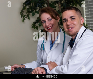 Deux friendly médecin travaillant ensemble à un bureau, sourire à la caméra. Banque D'Images