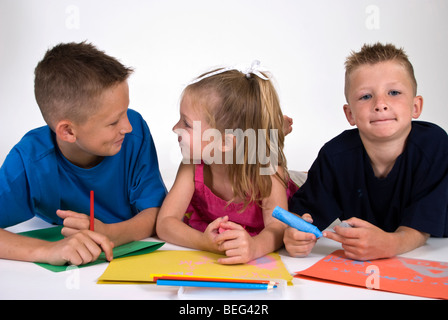 Trois enfants se trouvant sur le plancher sur la coloration du papier de couleur vive. Banque D'Images