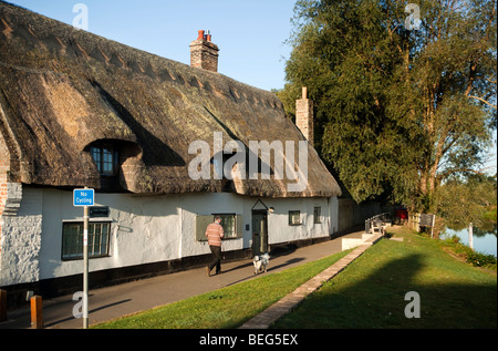 L'Angleterre, Cambridgeshire, Hemingford Grey, man walking dog riverside cottage de chaume idyllique passé Banque D'Images