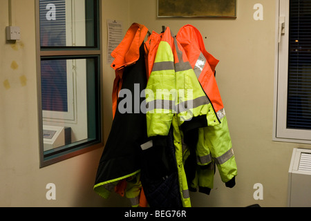 Gilets haute visibilité accrocher sur un étendoir appartenant au groupe de la sécurité côté piste (AOSU) le personnel de l'aéroport de Heathrow. Banque D'Images