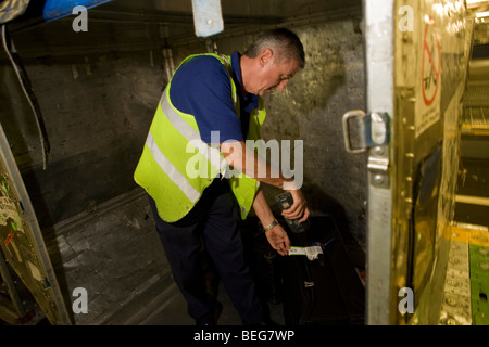 British Airways un bagagiste scanne le code barre de sa compagnie aérienne bagage du passager avant le chargement dans un récipient. Banque D'Images