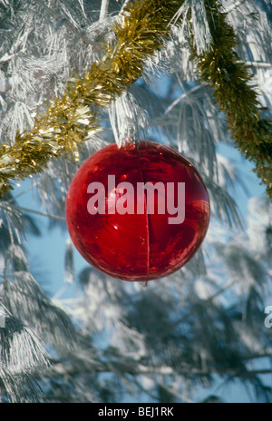 Ornement d'arbre de Noël en verre rouge avec des guirlandes sur un arbre d'extérieur floqué blanc sur un jour d'hiver ensoleillé dans la neige, Midwest USA Banque D'Images