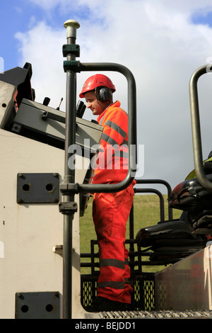 Homme portant une orange boiler suit et casque de sécurité l'exploitation d'une machine de décapage de la route Banque D'Images