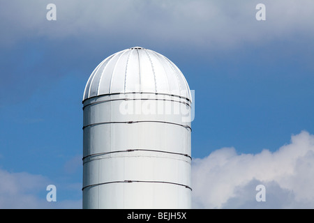 La moitié supérieure d'un silo blanc shot against a blue sky white puffy nuages blancs. Banque D'Images