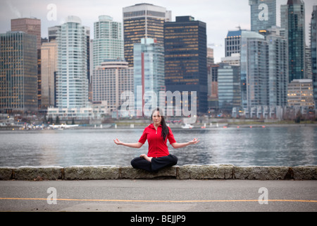 A Young Asian woman doing yoga sur la digue de Stanley Park avec le centre-ville au-delà, Vancouver, BC, Canada Banque D'Images