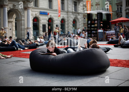 Un garçon se lit sur un coussin pouf à d'une bibliothèque dans la Hauptplatz dans la ville de Graz en Autriche Banque D'Images