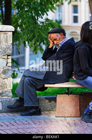 Vieil homme dormir dehors sur un banc dans une place de la ville. Banque D'Images