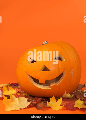 Citrouille souriante sculptée sur les feuilles d'automne coloré. Jack-o'-lantern Halloween symbole. Banque D'Images