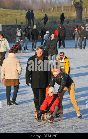 Mère fils poussant sur un traîneau et promeneurs marchant sur la glace de rivière gelée en hiver Banque D'Images