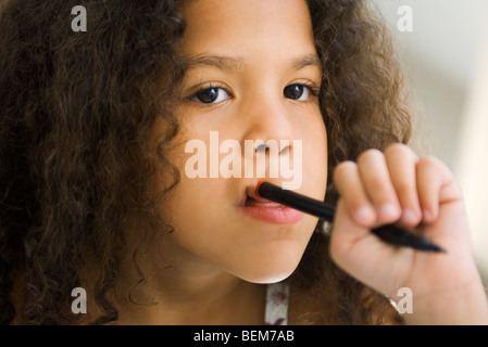 Little girl holding stylo contre la bouche, à l'écart Banque D'Images