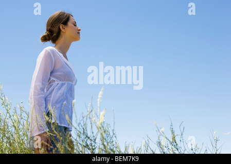 Jeune femme debout dans l'herbe haute, les yeux fermés, side view