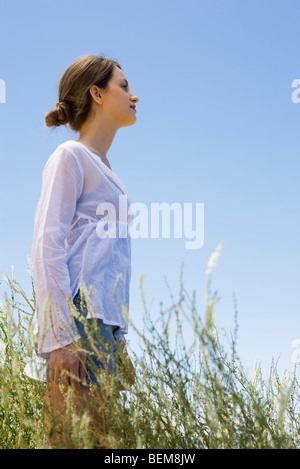 Jeune femme debout dans l'herbe haute, side view