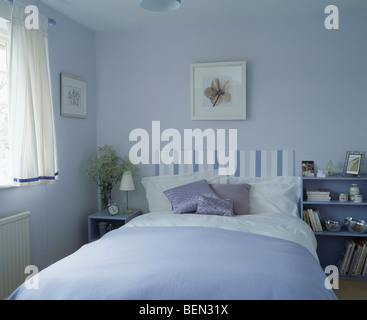 Tête de lit rembourrée à rayures sur lit avec coussins mauve et bleu pâle-couverture de lit en bleu pastel petite chambre avec des rideaux blancs Banque D'Images
