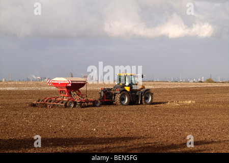 Un tracteur répandre des produits chimiques agricoles un champ de chaume à Cleveland UK avec chimique Teesside fonctionne en arrière-plan Banque D'Images