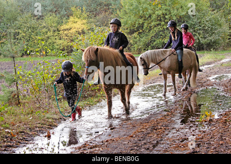 Enfants assis sur leurs poneys dans une flaque Banque D'Images