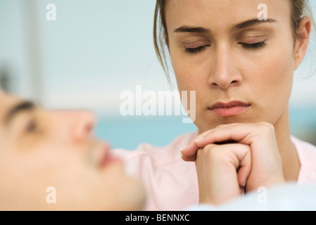 Femme assise à côté d'homme endormi, les mains jointes devant le visage, les yeux fermés Banque D'Images