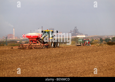 Un tracteur répandre des produits chimiques agricoles un champ de chaume à Cleveland UK avec l'aciérie Redcar en arrière-plan Banque D'Images