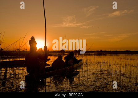 Les gens qui suivent le coucher du soleil sur un bateau mokoro dans le delta de l'Okavango, au Botswana, l'Afrique. Banque D'Images