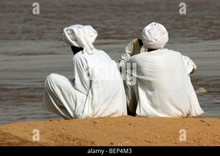 Deux hommes vêtus de blanc nubien thawbs / thobes / dishdashas assis sur les berges du Nil, au Soudan, en Afrique du Nord Banque D'Images