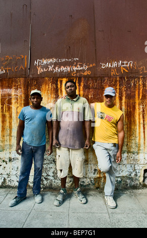 Trois jeunes travailleurs debout devant un mur rouillé regardant la caméra dans la vieille ville de La Havane. Banque D'Images