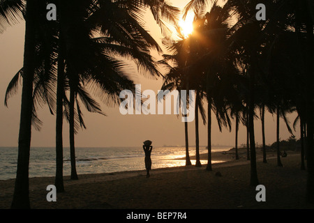 La silhouette des palmiers et femme transportant des marchandises sur la tête sur la plage au coucher du soleil, Golfe de Guinée, Lomé, Togo, Afrique de l'Ouest Banque D'Images