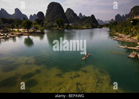 L'homme sur un radeau en bambou poussant vers le bas la rivière Li enroulement entre pics calcaires dans la région de Yangshuo, Chine Banque D'Images