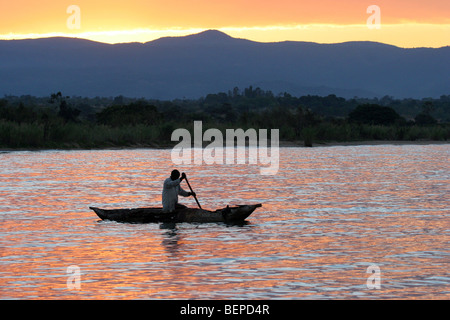 Pêcheur noir dans le bateau de pêche en bois / proa pagayer sur le lac Malawi au coucher du soleil, le Malawi, l'Afrique Banque D'Images