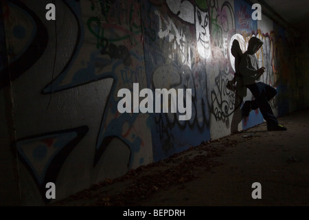 Un adolescent de pulvériser un graffiti sur un mur dans une ruelle Banque D'Images