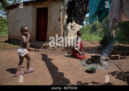 L'Ouganda, une jeune femme Proscovia, et son bébé Saifa (3), la cuisson sur un feu ouvert en face de sa petite chambre. Kayunga District. Banque D'Images