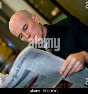 Portrait d'un homme chauve à la fin de années 40, le port d'un costume foncé lire un journal. Banque D'Images