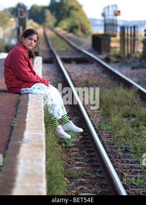 Jeune fille s'assit sur le bord du quai de la gare en attendant le train. Banque D'Images