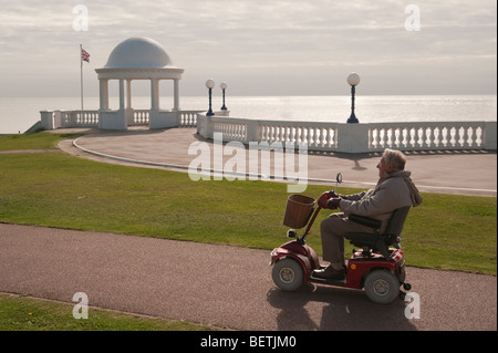 Vieil homme entraîne un scooter de mobilité électrique près du front de mer sur Bexhill East Sussex England UK Banque D'Images