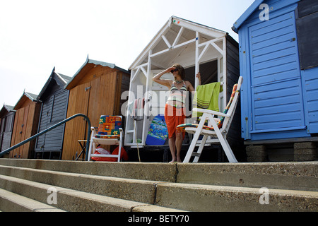 Femme debout à l'extérieur d'une plage anglaise hut typiquement sur une journée d'été Anglais Banque D'Images