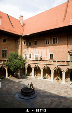 Père et fille touristiques s'asseoir sur le puits d'eau dans la cour du Grand Collège, ou Collegium Maius. Cracovie, Pologne. Banque D'Images