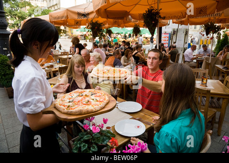 Serveuse sert des pizzas pour les jeunes touristes anglais assis à une table de restaurant. Marché / Markt. Cracovie. La Pologne. Banque D'Images