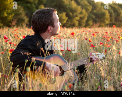 Jeune homme jouant de la guitare dans champ de coquelicots sur le coucher du soleil Banque D'Images