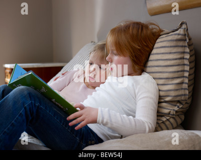 Deux sœurs s'asseoir la lecture sur un lit simple Banque D'Images